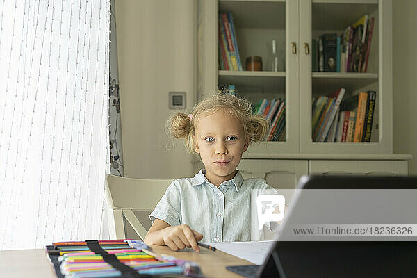 Überraschtes blondes Mädchen benutzt Laptop am Schreibtisch