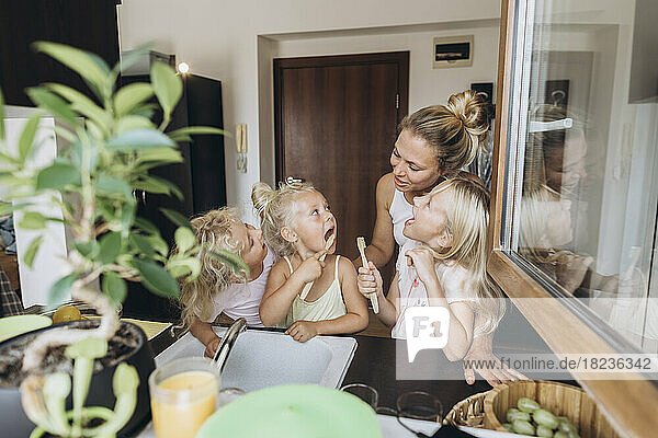 Mother watching daughters brushing their teeth with wooden brushes in the kitchen