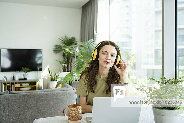 Smiling freelancer wearing wireless headphones looking at laptop
