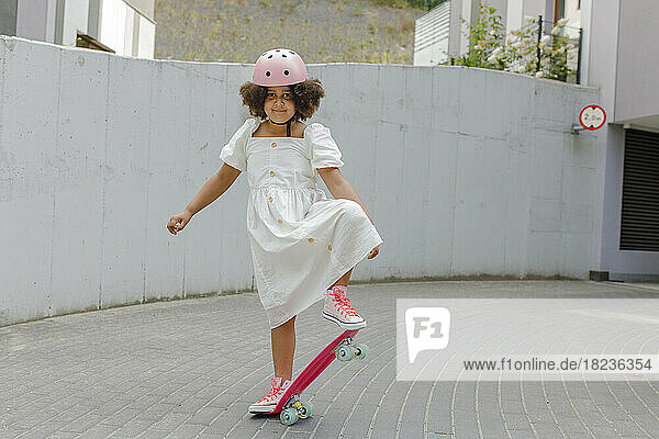 Smiling girl wearing helmet skateboarding on footpath