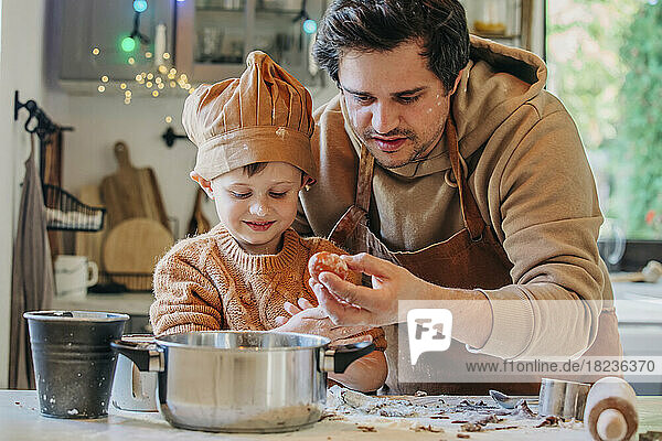 Smiling son cooking with father holding egg at table in kitchen