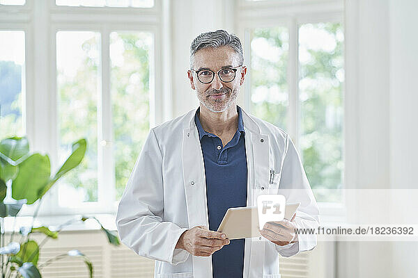 Smiling doctor standing with tablet PC in medical practice