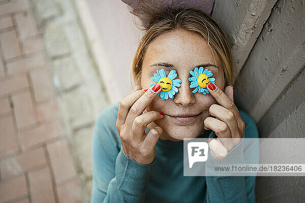 Lächelnde junge Frau hält künstliche Blume über die Augen
