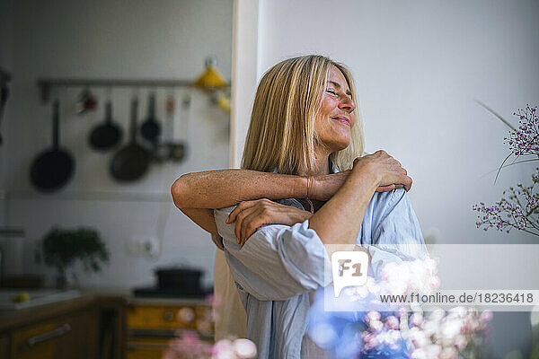 Smiling blond woman with friend embracing her from behind at home