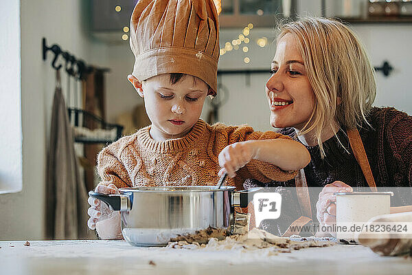 Glückliche blonde Frau mit Sohn bereitet zu Hause Kekse auf dem Tisch zu