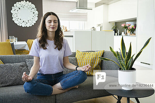 Woman with eyes closed meditating on sofa at home