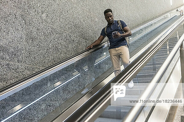 Mann benutzt Mobiltelefon und bewegt sich auf Rolltreppe nach unten