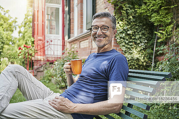 Happy man with coffee cup sitting on bench in back yard