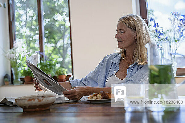Mature woman reading newspaper with food at table