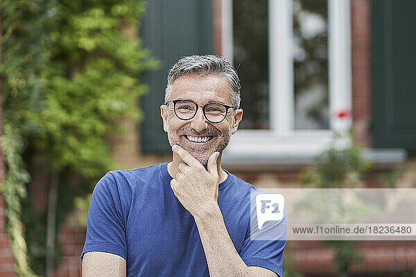 Smiling man wearing eyeglasses with hand on chin in front of house