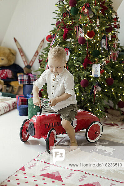 Boy playing with toy car near Christmas tree at home