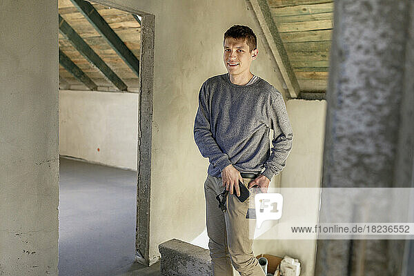 Smiling young man holding trowel and smart phone at home