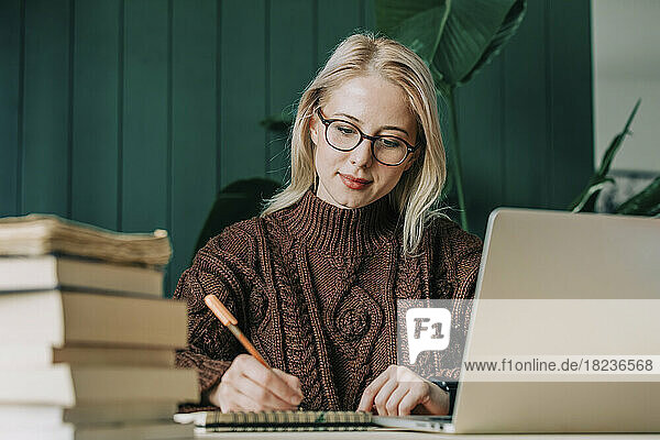 Businesswoman wearing eyeglasses writing in diary at home office