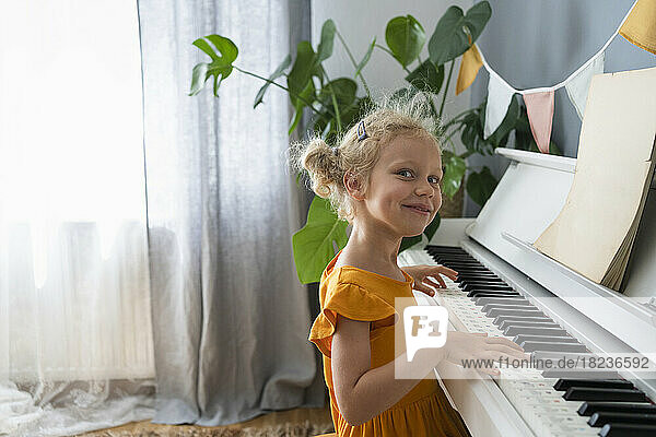 Smiling blond girl playing piano at home