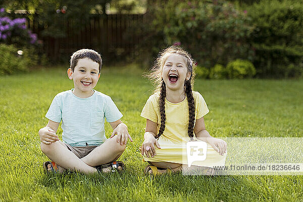 Cheerful girl sitting with brother on grass in back yard