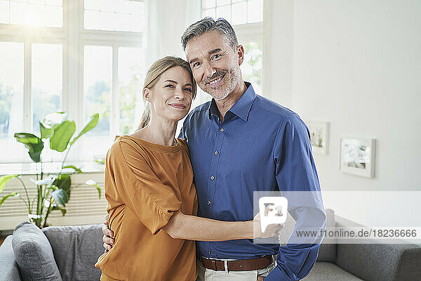 Smiling couple embracing in front of sofa at home