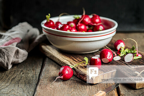 Fresh radishes in bowl on cutting board at table