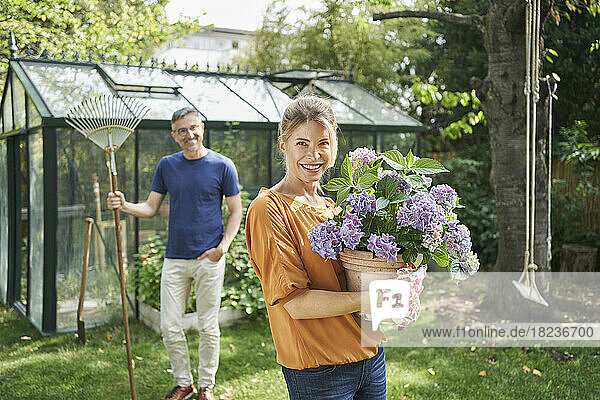 Smiling woman holding potted plant with man in background at back yard