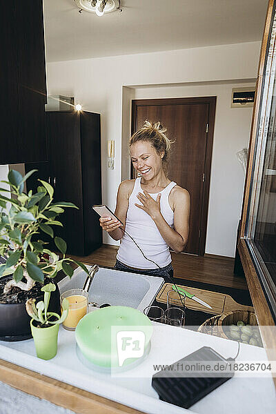 Happy woman looking at mobile phone in the kitchen