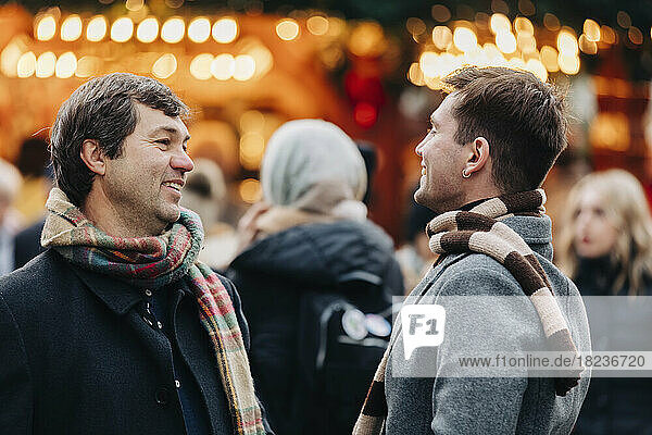 Lächelnder Mann im Gespräch mit Vater  der auf dem Weihnachtsmarkt steht