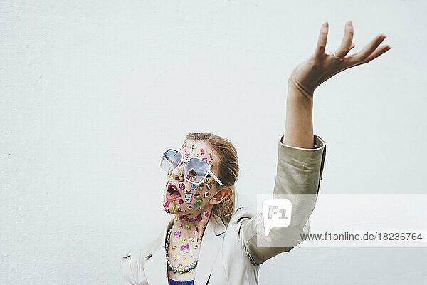 Woman with colorful stickers on face gesturing in front of white background