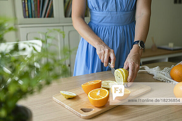 Hands of woman cutting lemons and oranges on table at home