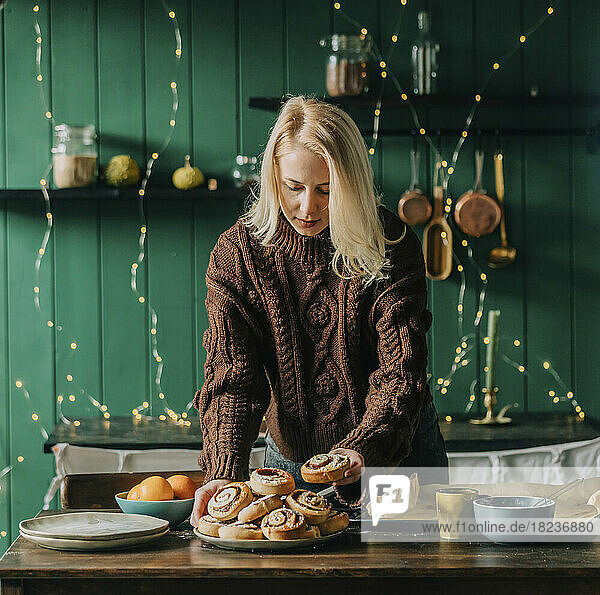 Woman arranging cinnamon buns on plate on table at home