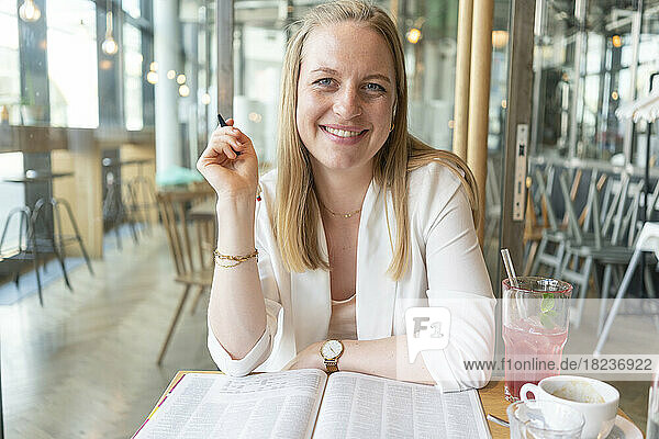 Happy businesswoman with magazine sitting at table in cafe