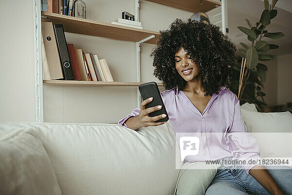 Young woman with Afro hairstyle using mobile phone in living room