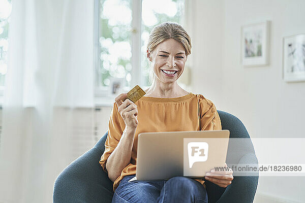 Happy woman with credit card doing online shopping through laptop at home