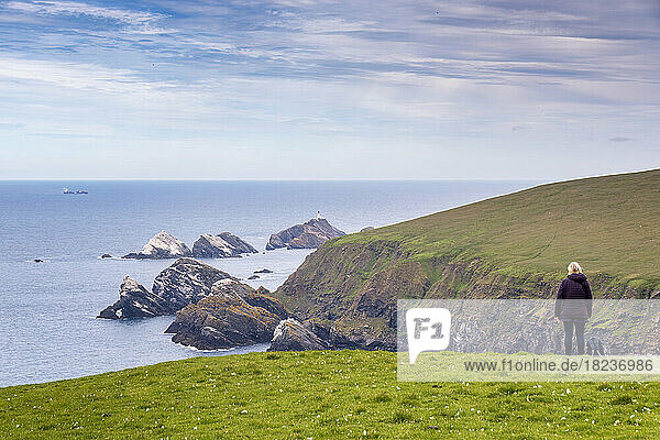 UK  Scotland  Unst  Female hiker standing on clifftop looking toward Muckle Flugga Lighthouse