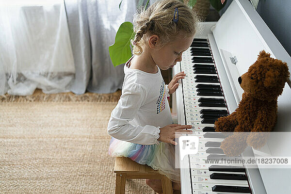 Mädchen lernt zu Hause mit Teddybär Klavier spielen