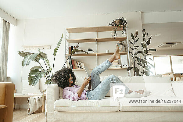 Happy woman using laptop lying on sofa in living room