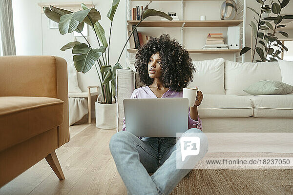 Contemplative woman with coffee cup and laptop at home