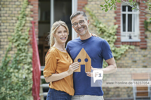 Happy couple holding wooden house model in garden