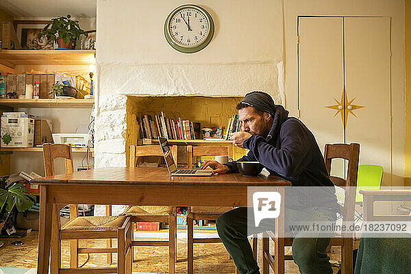 Freelancer eating meal using laptop at desk in home
