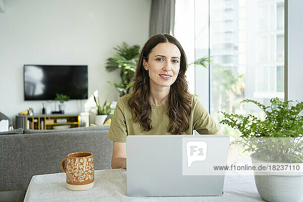 Smiling freelancer with laptop on table at home