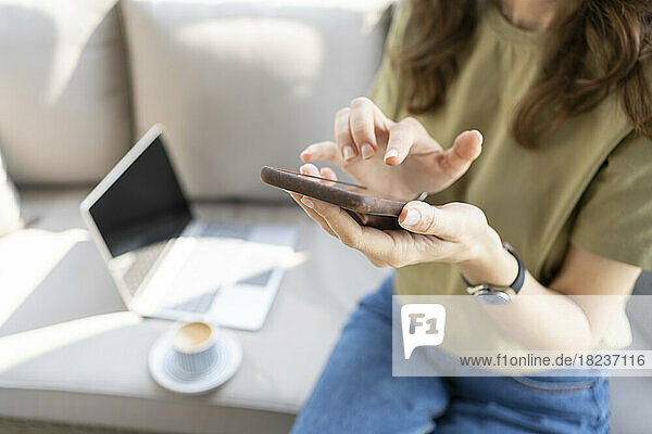 Hands of freelancer using smart phone on sofa