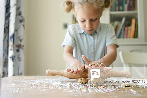 Girl rolling cookie dough on table at home