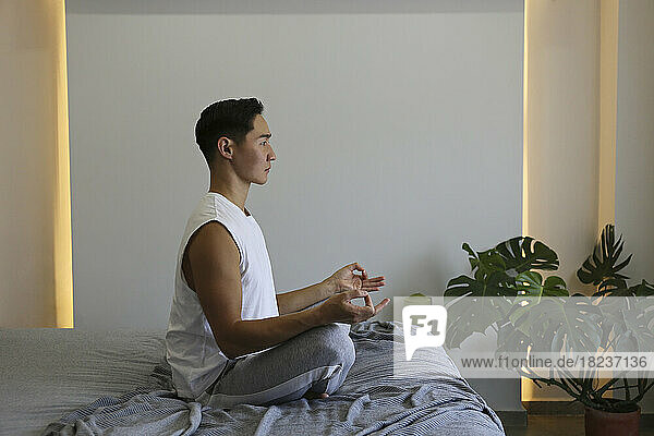 Young man practicing yoga sitting on bed at home