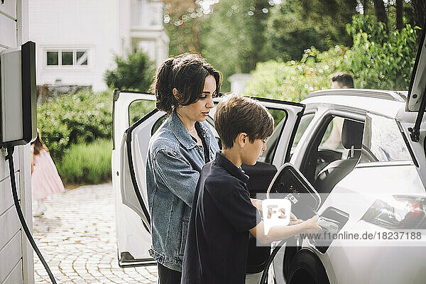 Seitenansicht von Mutter und Sohn beim Aufladen eines Elektroautos vor dem Haus