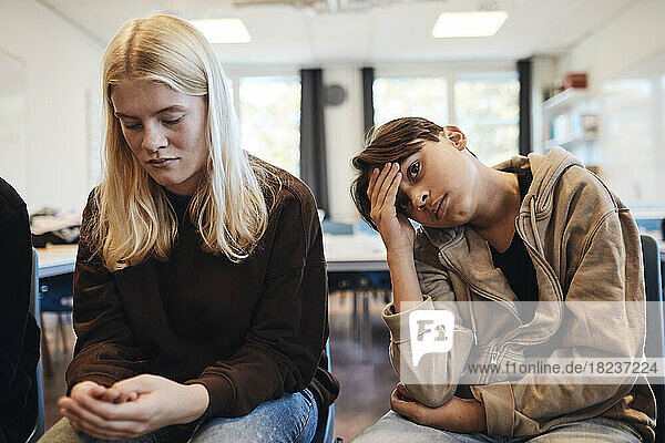 Trauriger Teenager  der während der Therapie bei einem blonden Mädchen im Klassenzimmer sitzt