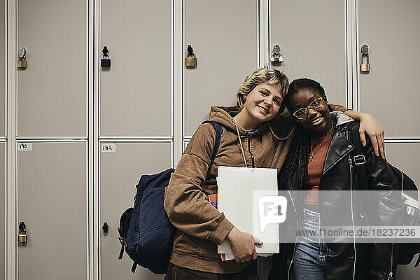 Porträt von lächelnden Freundinnen  die zusammen vor einem Spind in der Schule stehen