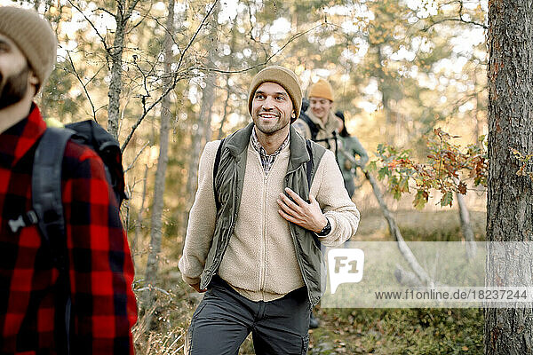 Lächelnder Mann in warmer Kleidung beim Wandern mit Freunden im Wald
