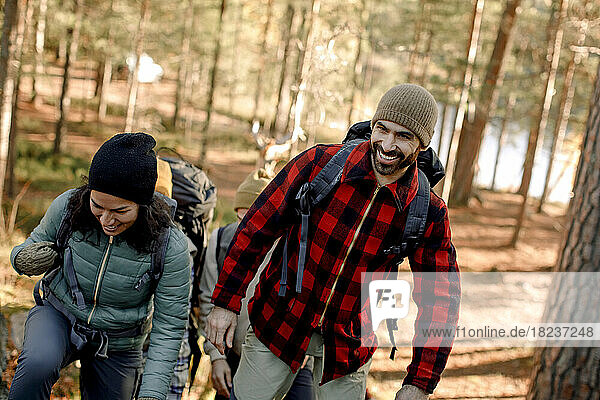 Glücklicher Mann mit kariertem Hemd beim Wandern mit einer Freundin im Wald