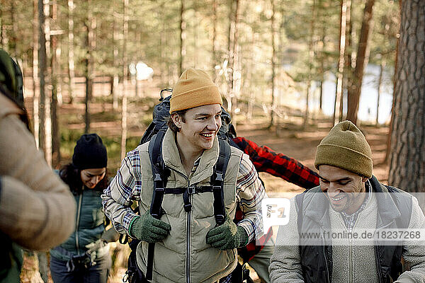 Happy young man talking to male friend while hiking in forest