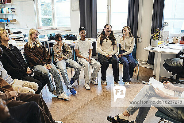 Glückliche Schülerinnen und Schüler sitzen mit einem Berater in einer Gruppentherapie in der Schule