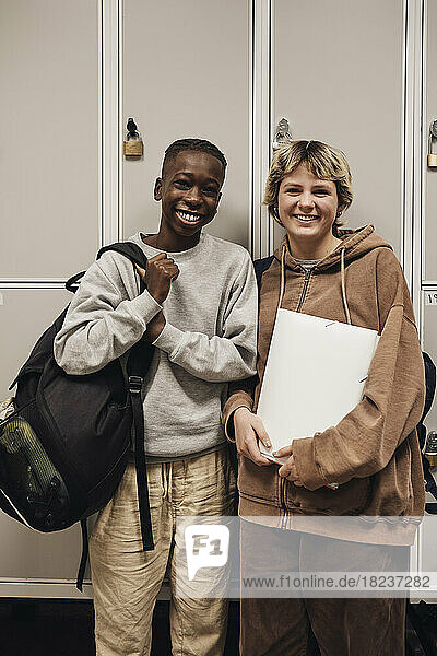 Porträt eines glücklichen Teenagers und eines Mädchens  die vor einem Spind in der Schule stehen