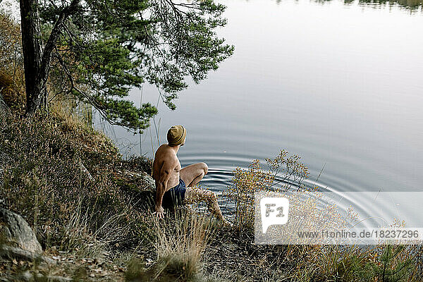 Hoher Blickwinkel eines am Seeufer sitzenden Mannes ohne Hemd