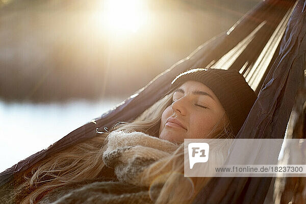 Junge Frau mit geschlossenen Augen entspannt sich in der Hängematte an einem sonnigen Tag
